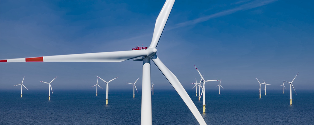 Photograph of wind turbines spinning in sea against blue sky.
