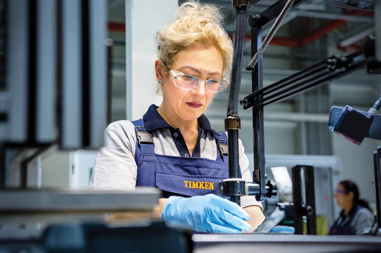 A woman wearing safety glasses assembles part at a work bench