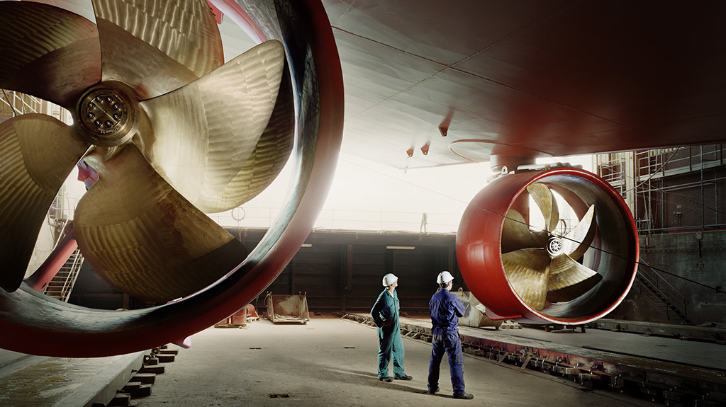 Two people inspecting the propellers of a large cargo ship.