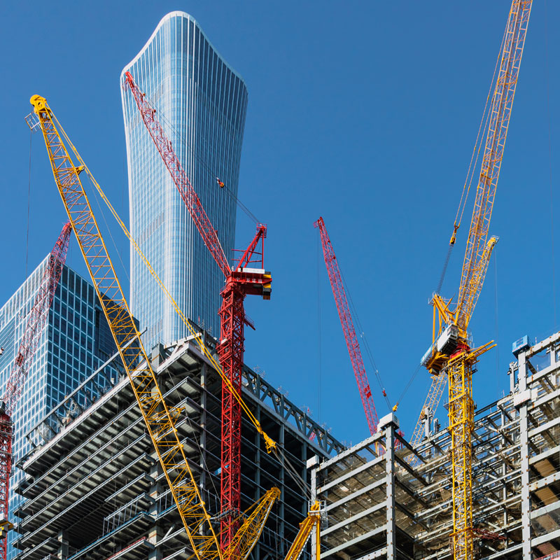 Multiple yellow and red construction cranes operating around the steel skeleton of a new skyscraper.